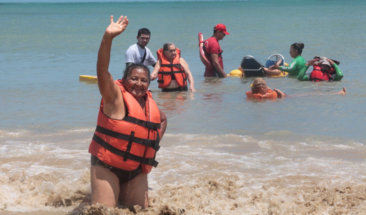 Dona Ana Maria acena para a câmera na beira da praia